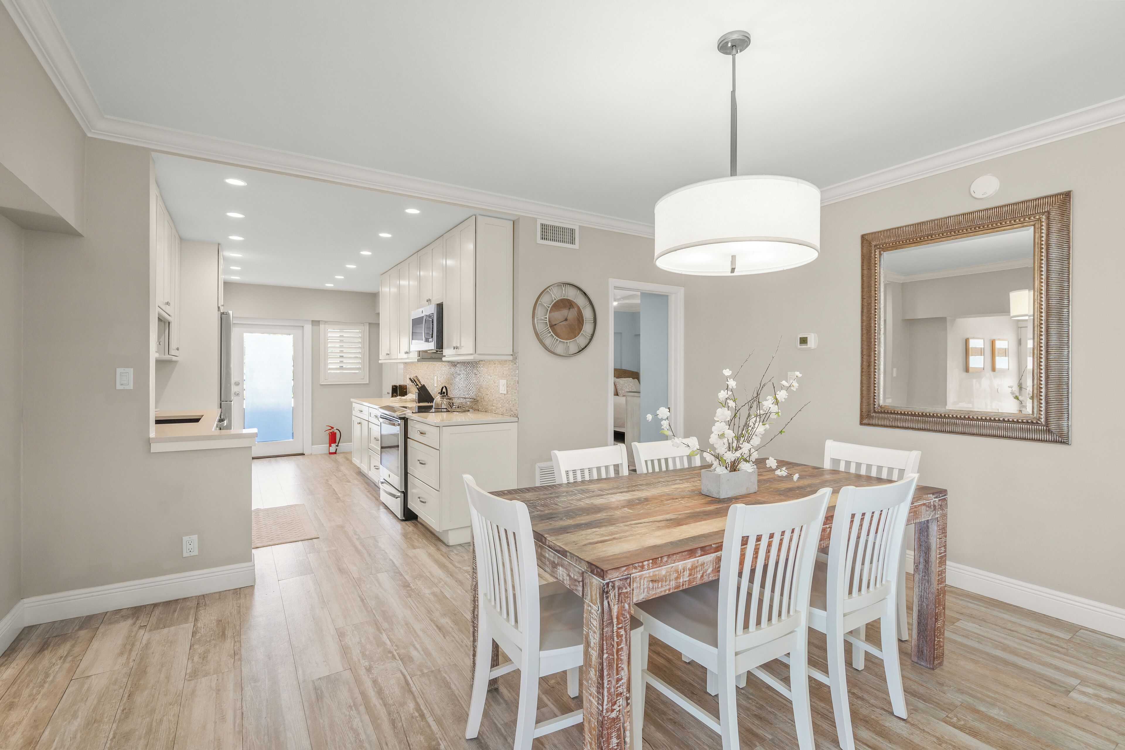 A modern kitchen with white cabinets, a wooden dining table, and a large mirror.