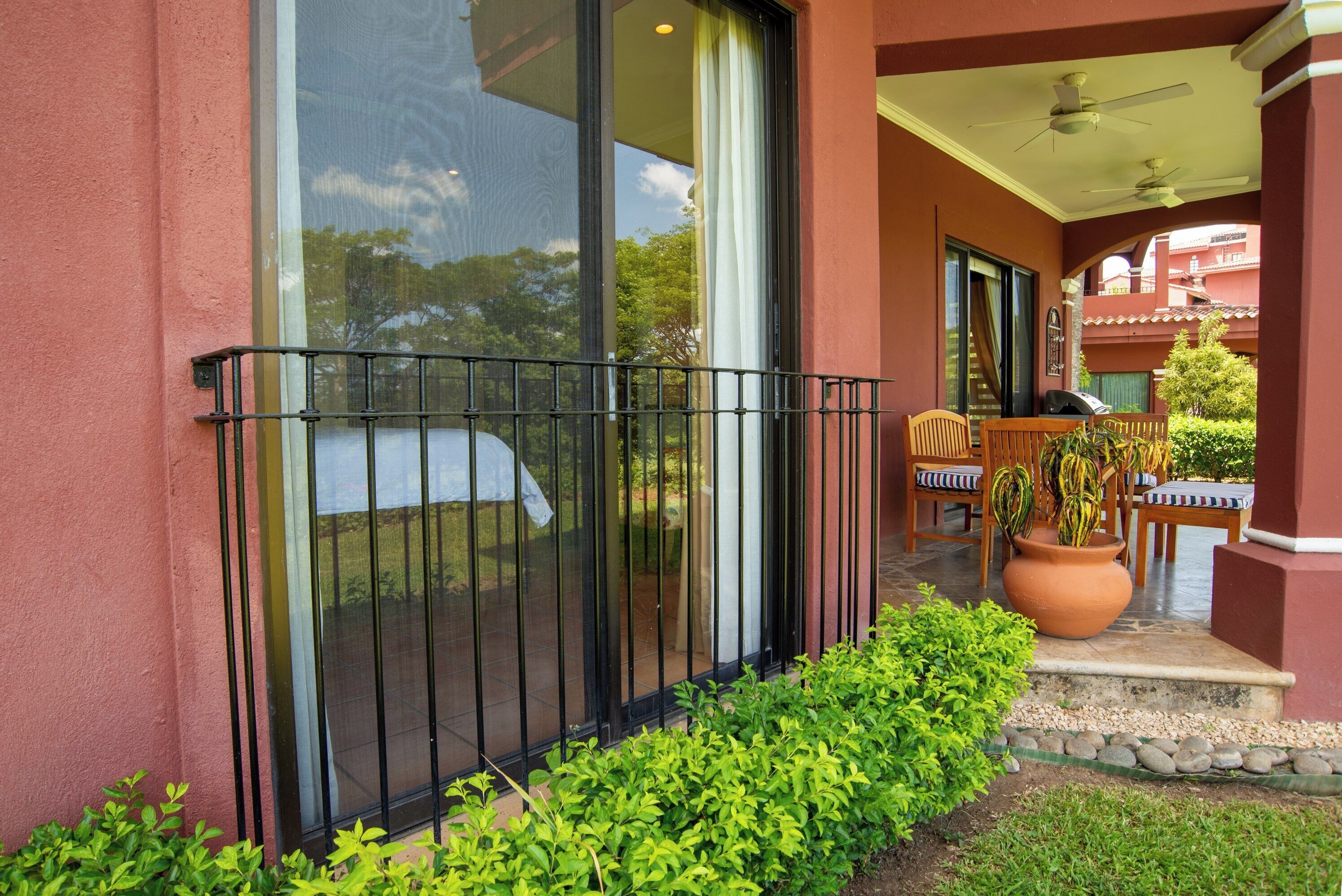 A balcony with a black metal railing, a wooden chair, a table, and a potted plant.