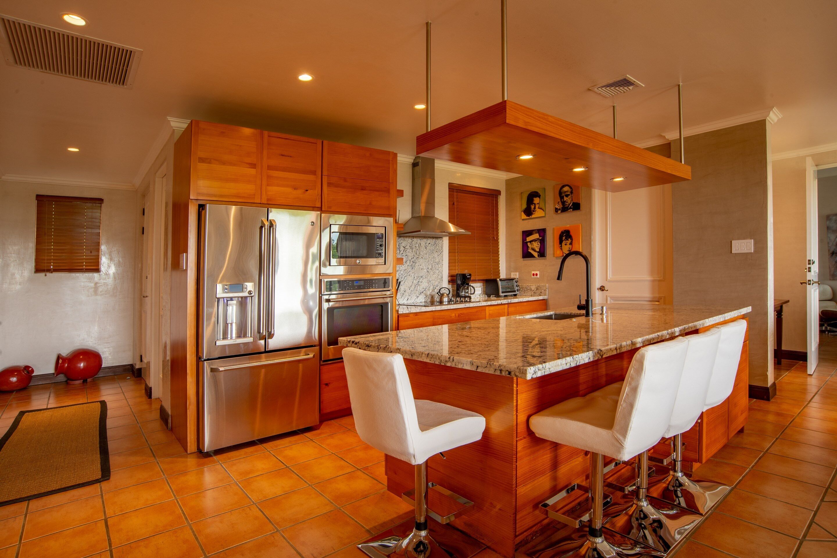 A modern kitchen with stainless steel appliances, wooden cabinets, and a bar area with white bar stools.