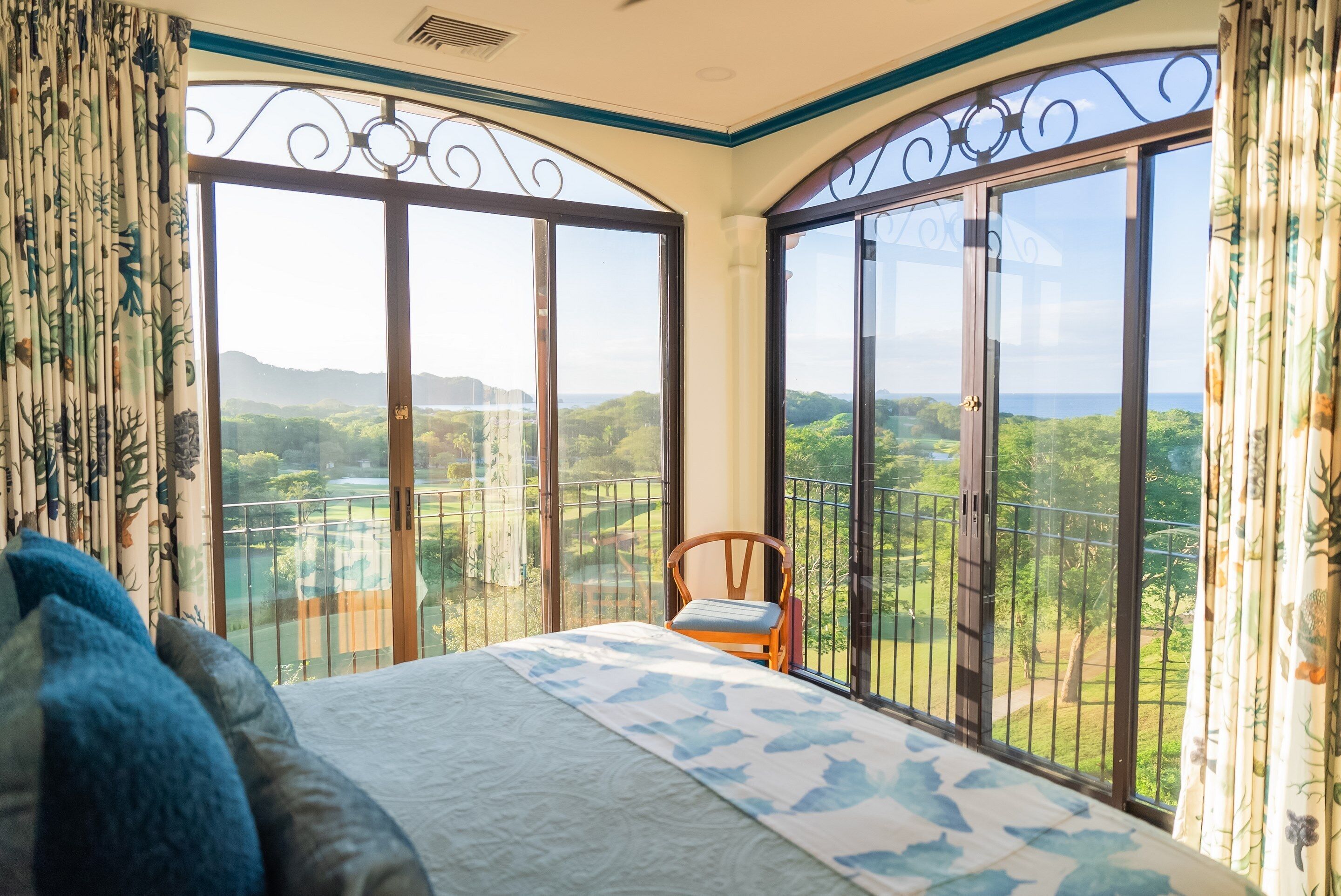 A bedroom with a large bed, a chair, and a balcony with a scenic view.
