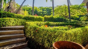 Un jardín con una escalera de piedra, setos bien cuidados y una gran maceta de terracota.