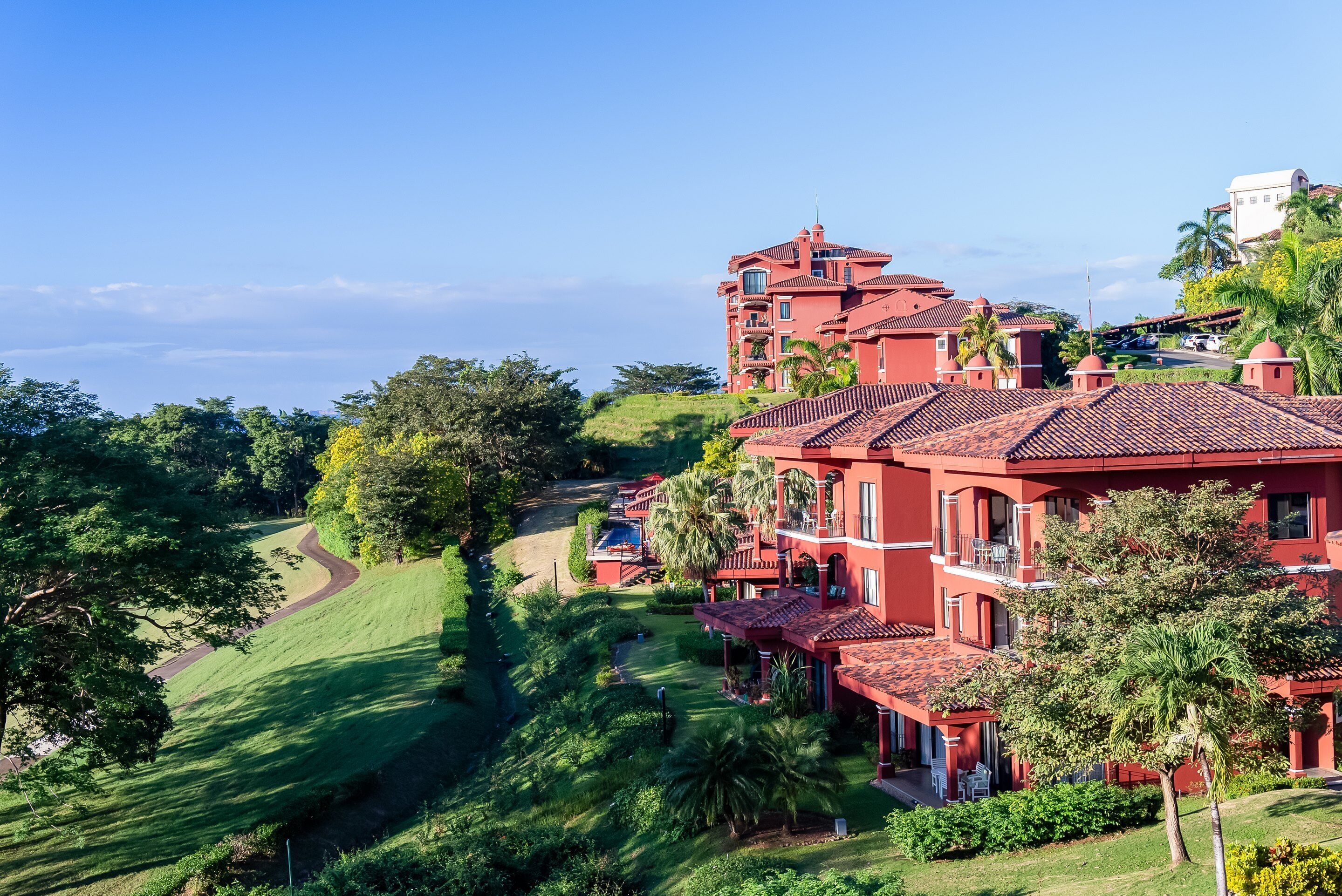 Un hotel de varios pisos con tejados de tejas rojas, exuberante vegetación y vistas despejadas de las colinas circundantes.