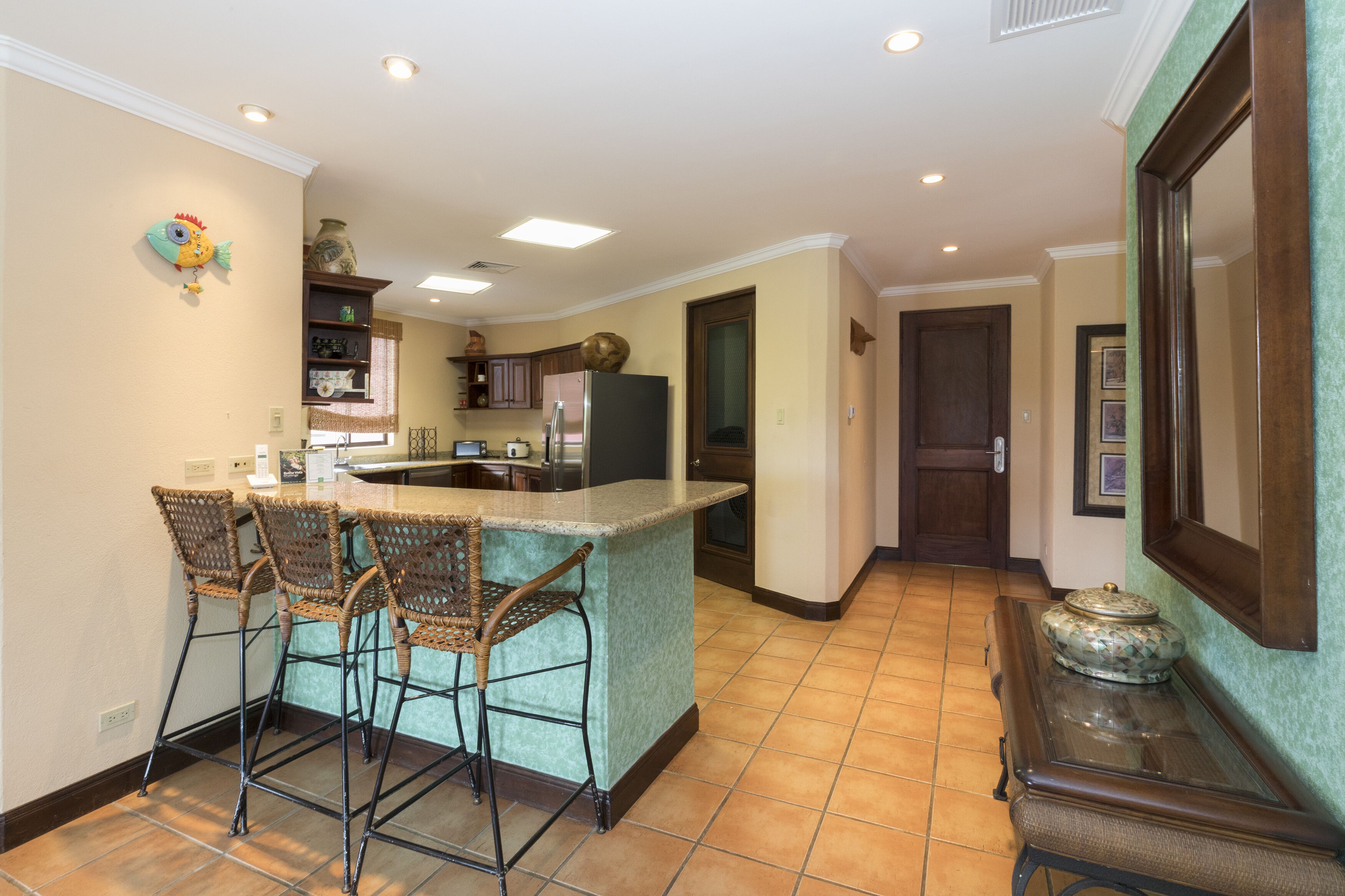 A kitchen with a bar area, wicker chairs, a refrigerator, and a decorative fish on the wall.