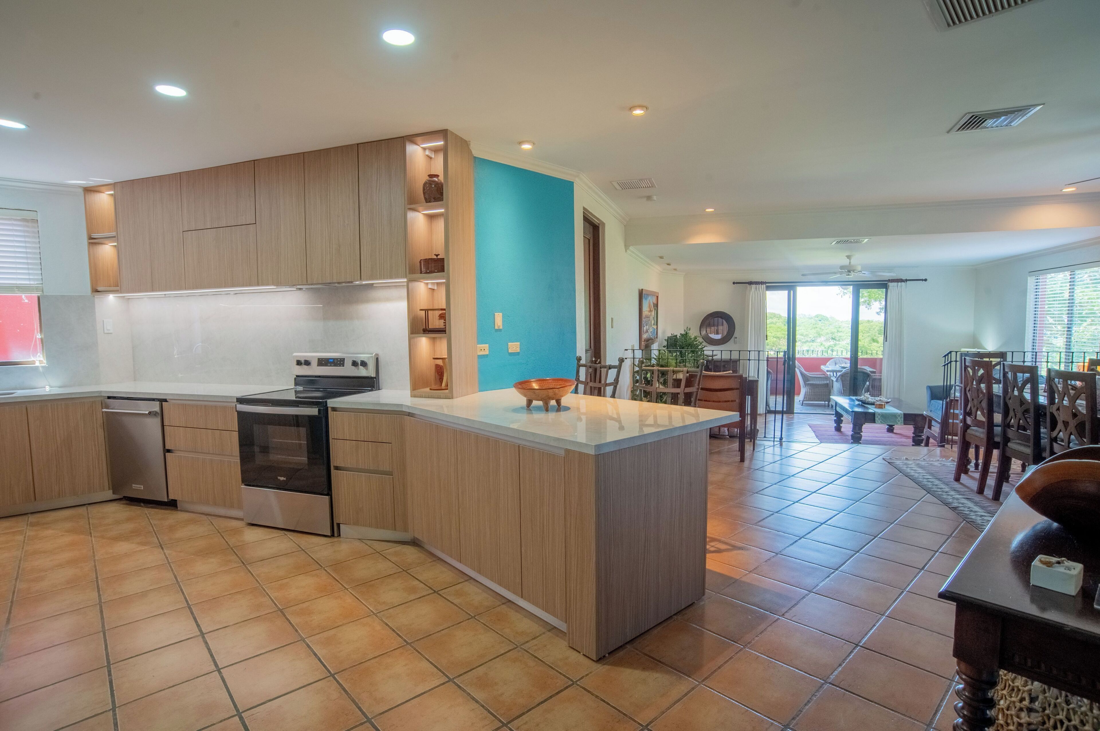 A modern kitchen with wooden cabinets, a central island, and a dining area with a view.