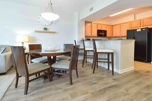 Una cocina moderna con armarios de madera, un refrigerador negro y un microondas. Hay una zona de comedor con una mesa redonda y sillas.