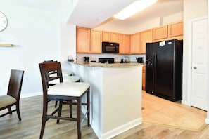 Una cocina con armarios de madera, un refrigerador negro, un microondas y una pequeña isla con una silla.