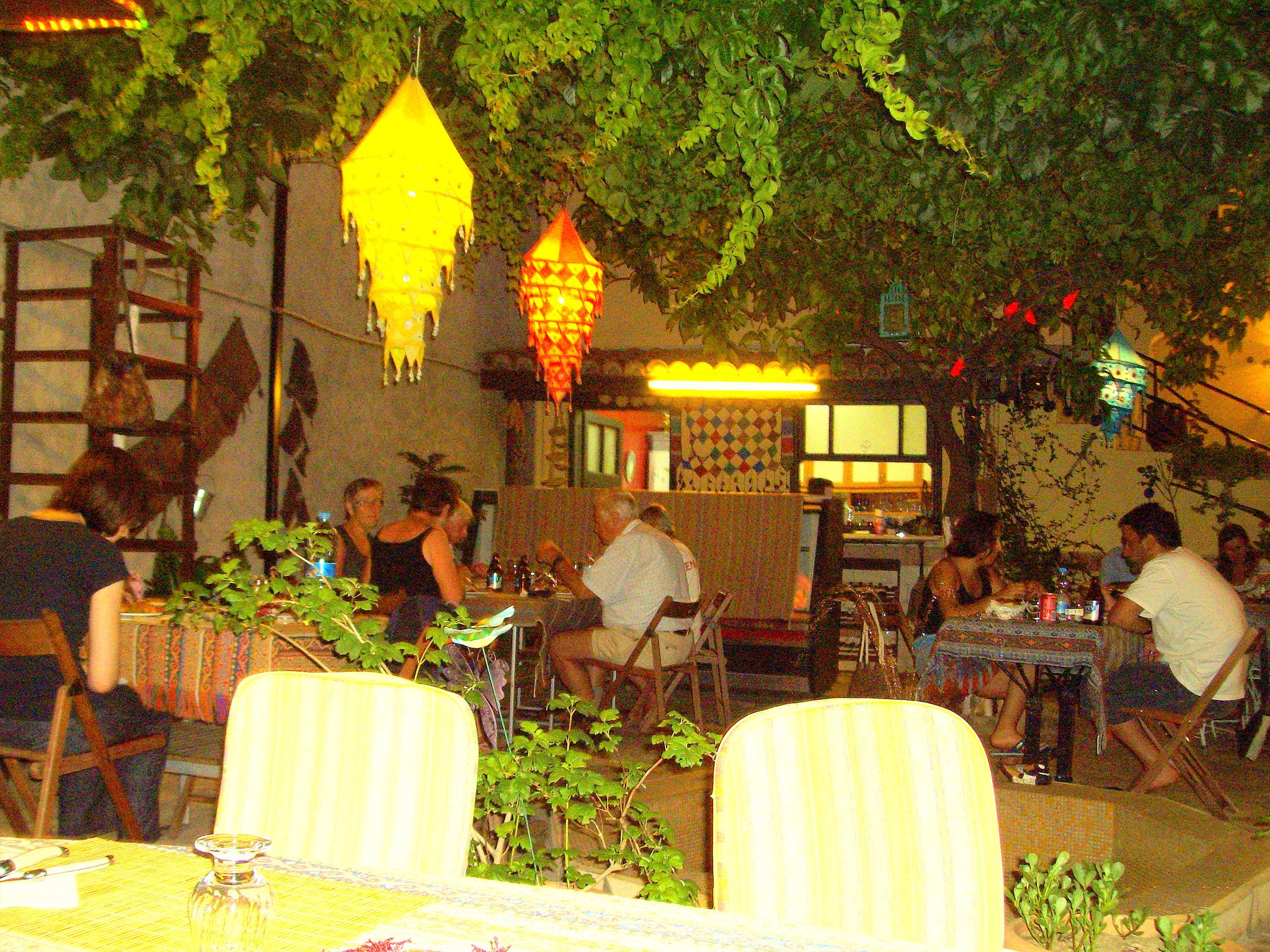 Un espace de restauration en plein air, avec des tables et des chaises, entouré de verdure et agrémenté de lanternes suspendues.