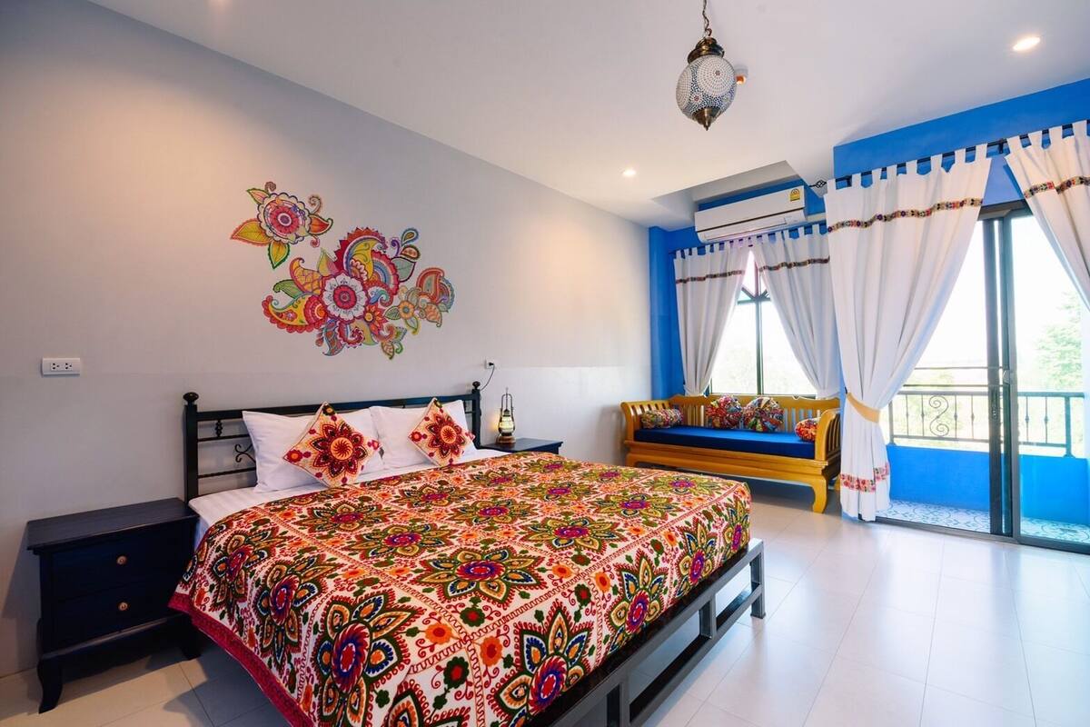 A bedroom with a bed, bedside table, wall art, and a balcony with a sofa.