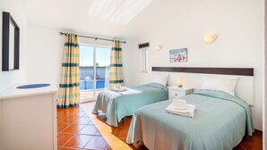 A hotel room with two beds, a desk, a small table, and a view of a swimming pool. - Casa Giovanna Praia da Luz 3 bedrooms, aircon, solar heated pool & sea view. (Luz)