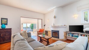 A living room with a fireplace, a television, and a bookshelf. - Casa Giovanna Praia da Luz 3 bedrooms, aircon, solar heated pool & sea view. (Luz)