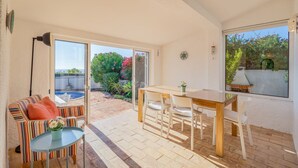 A room with a dining table and chairs, a striped sofa, a small table with a vase, and a view of a pool and garden through a glass door. - Casa Giovanna Praia da Luz 3 bedrooms, aircon, solar heated pool & sea view. (Luz)