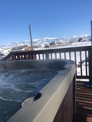 A hot tub on a wooden deck with a view of snow-covered mountains.