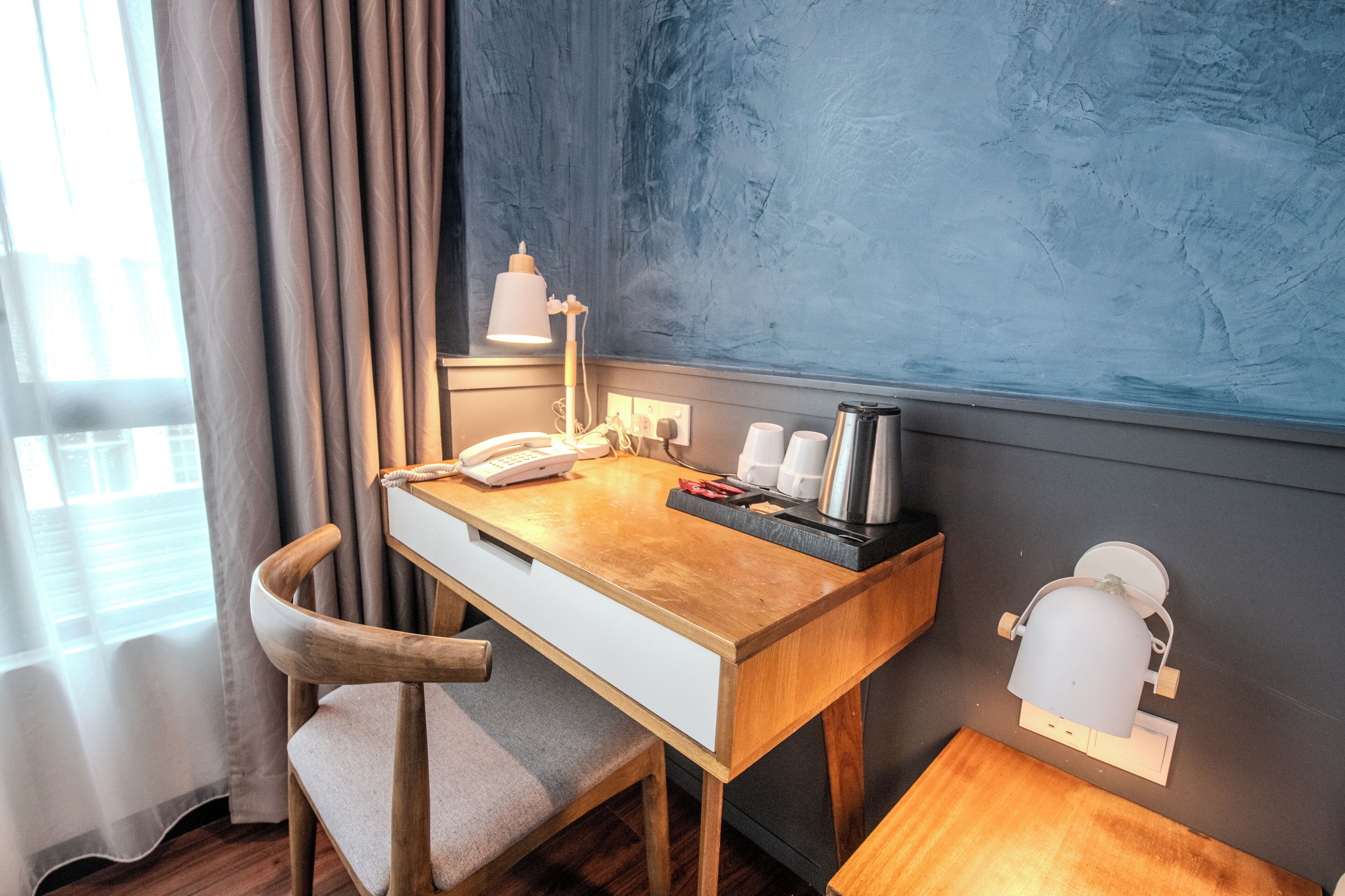 Una habitación de hotel compacta con un escritorio de madera, un teléfono, una cafetera y una pequeña mesa.