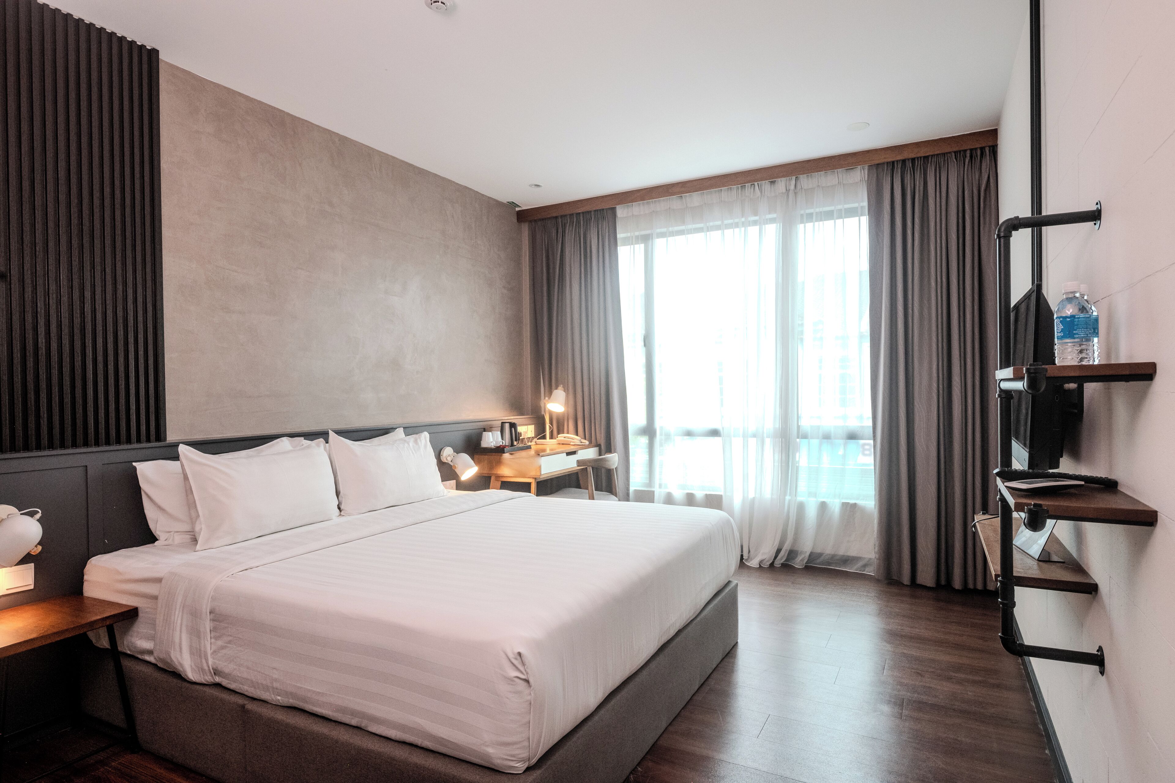 Une chambre d’hôtel avec un grand lit, des tables de chevet, un bureau, une télévision et une fenêtre avec des rideaux.