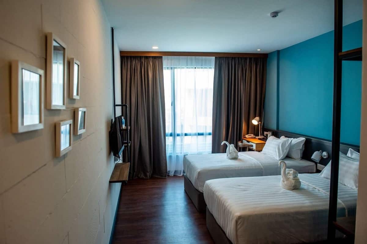 A hotel room with two beds, a desk with a lamp, a TV, and a window with curtains.