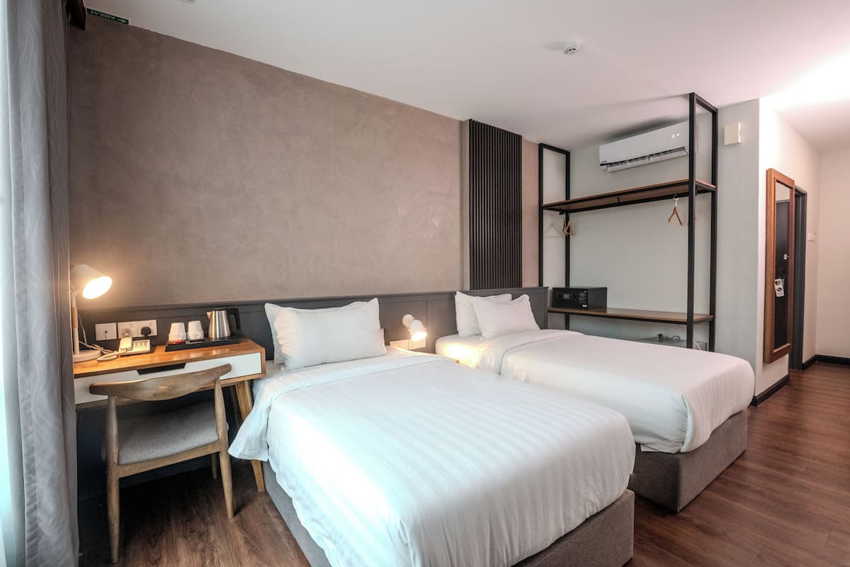 A hotel room with two beds, a desk with a chair, a mirror, and an air conditioning unit.