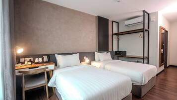 A hotel room with two beds, a desk with a chair, a mirror, and an air conditioning unit.
