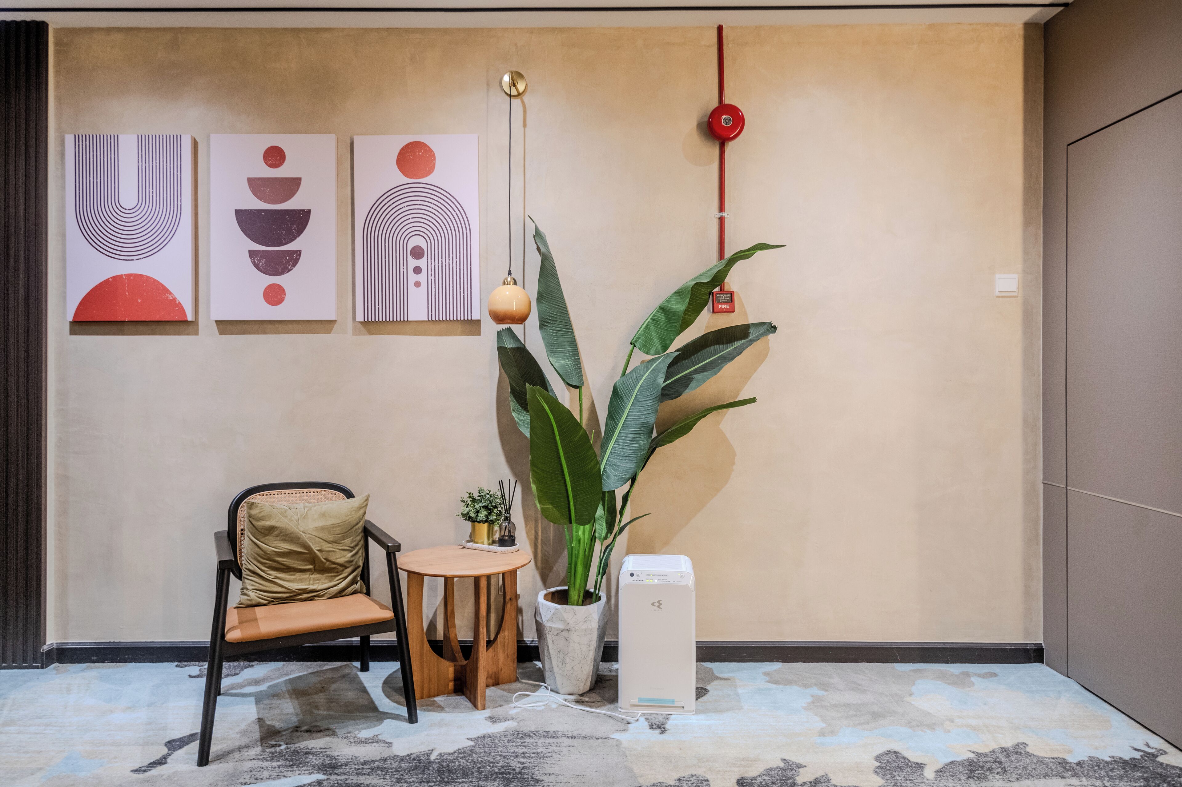 A modern room with a minimalist design, featuring a chair, a small table, a potted plant, and a white device on the floor.