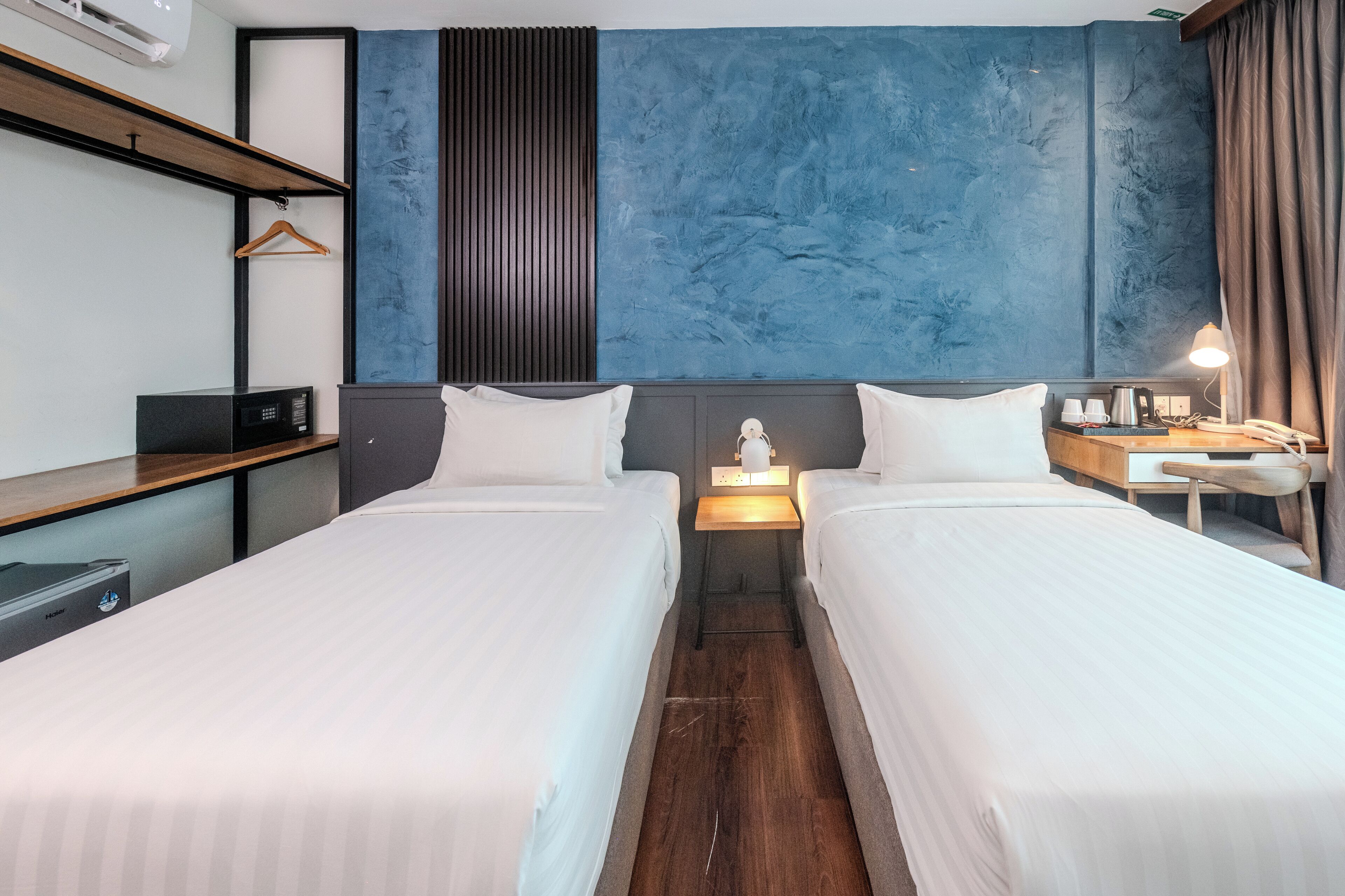 A hotel room with two beds, a desk, a chair, a nightstand, a lamp, and a wardrobe.