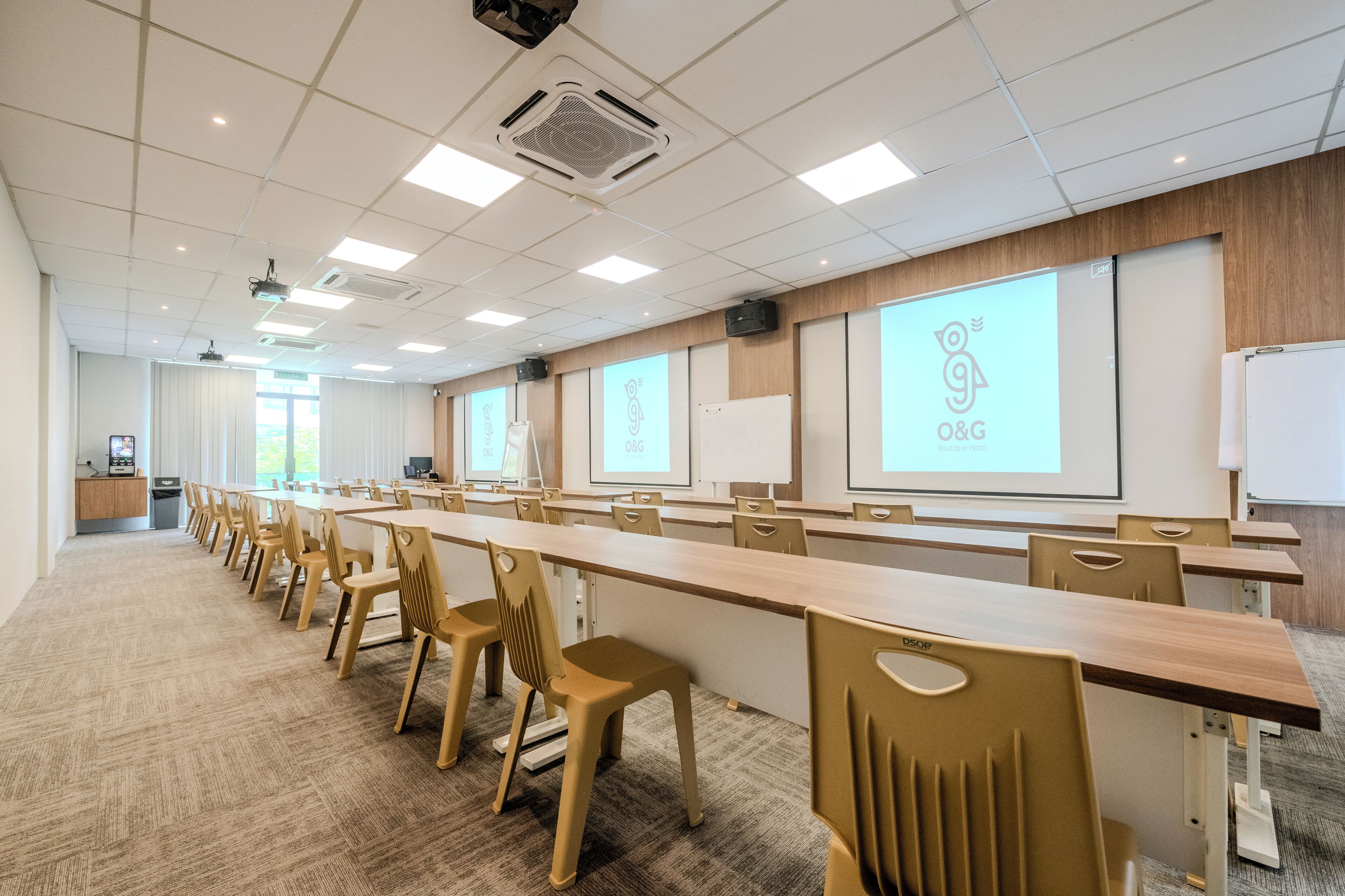 A conference room with a long table, chairs, a whiteboard, and a projector screen displaying a logo.