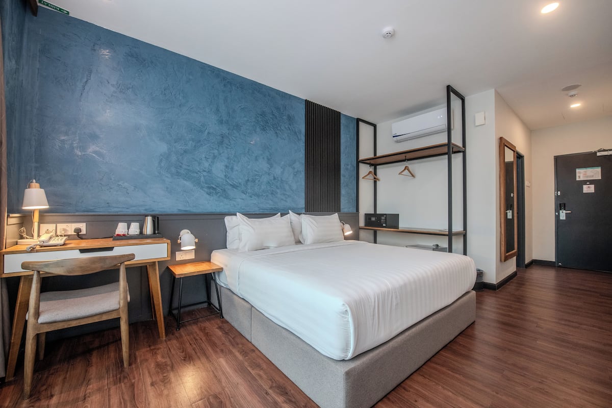 A modern hotel room with a large bed, a desk with a chair, a wardrobe, and an air conditioning unit.