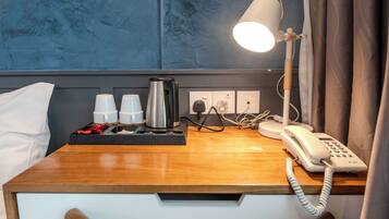 Une chambre d’hôtel avec un bureau en bois, une lampe de chevet, un téléphone et un plateau avec des tasses et une cafetière.