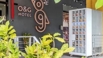 A hotel entrance with a neon sign, a vending machine, and potted plants.