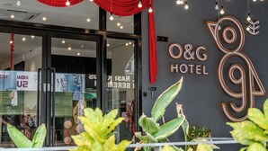 Exterior do Hotel O&G com design moderno, apresentando uma grande placa iluminada, portas de vidro e interior visível pelas janelas.