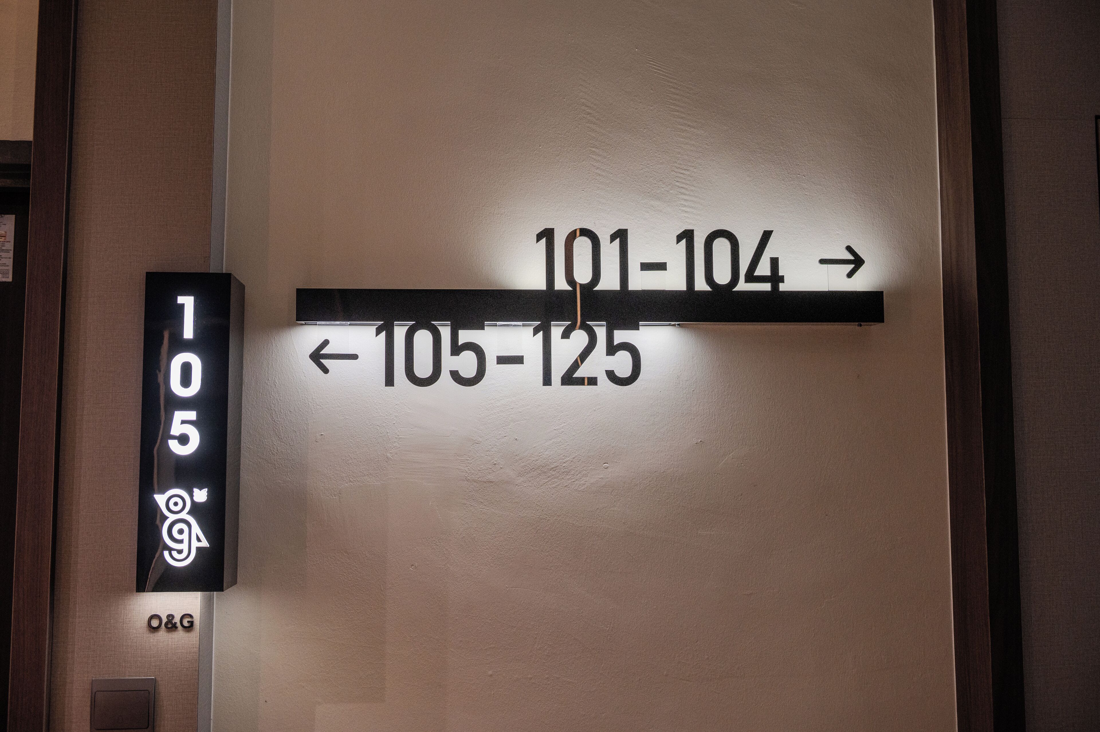 A wall-mounted sign with directional arrows and room numbers, indicating hotel room assignments.