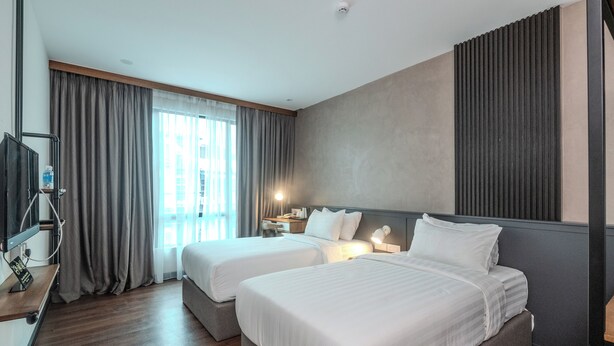 Quarto de hotel com duas camas, uma escrivaninha, uma televisão e uma janela grande com cortinas.