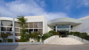 A modern building with a curved facade, large windows, and a set of stairs leading to the entrance. - Happy Days (Rhodes)