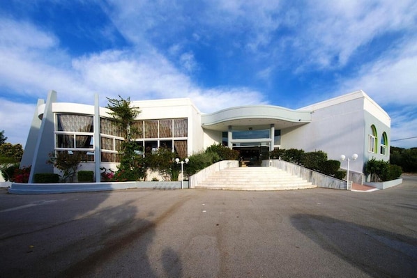 A modern building with a curved facade, large windows, and a central entrance with steps. - Happy Days (Rhodes)