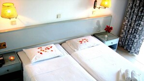 A hotel room with two beds, each with white linens and pillows, a bedside table with a lamp, and a nightstand with a radio. - Happy Days (Rhodes)