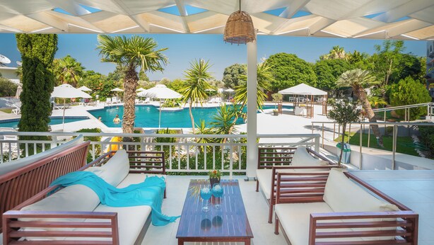 Eine Dachterrasse mit Blick auf einen Pool, Sitzgelegenheiten im Freien und einer Pergola mit Sonnenschirmen.