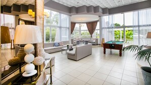 Ein geräumiger Wohnbereich mit Pooltisch, Sofas und großen Fenstern mit Blick auf Grünflächen.