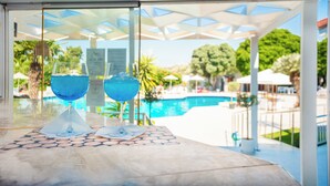 Eine Poolbar mit zwei blauen Cocktails auf einem Marmortisch, mit Blick auf einen Pool und üppiges Grün.