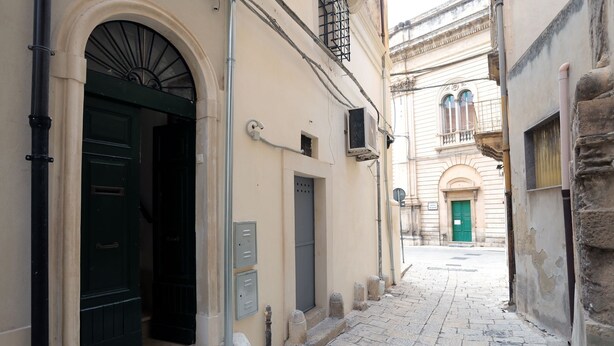 A narrow cobblestone street with buildings on either side, featuring arched doorways and traditional architecture. - Casa Marinella (Scicli)