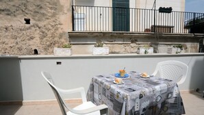 A terrace with a table set for two, white plastic chairs, and potted plants on a balcony. - Casa Marinella (Scicli)