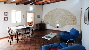A living room with a dining area, a stone wall, and a blue armchair. - Casa Marinella (Scicli)