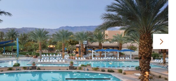 Relax by the pool surrounded by palm trees and lounge chairs in a scenic mountain setting.
