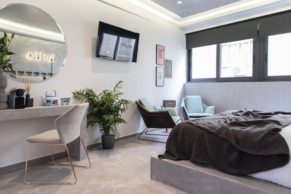 A modern bedroom with a bed, a desk with a computer, a chair, a large mirror, and a TV.