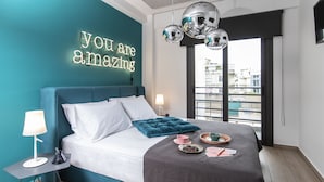 A modern bedroom with a teal accent wall, a bed with white and teal bedding, a bedside table with a lamp, and a neon sign. - 14 Reasons Why (Athens)