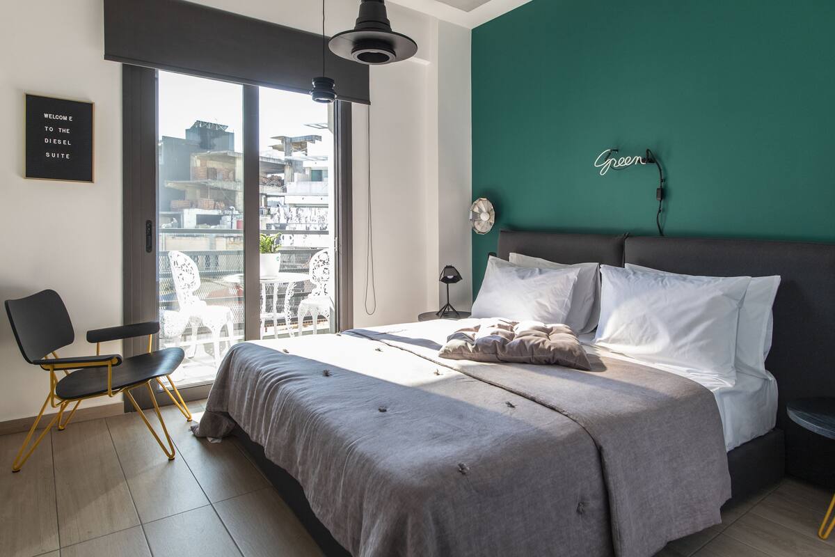 A modern bedroom with a bed, a chair, a bedside table, a lamp, and a view of the city through a large window.