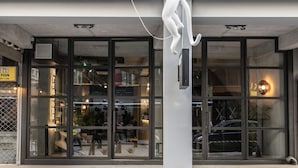 A building facade with a large glass entrance, a white sculpture of a figure holding a ball, and a sign with the number 14. - 14 Reasons Why (Athens)