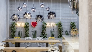 A modern dining area with a wooden table, geometric chairs, hanging spherical light fixtures, and a neon sign with a heart shape. - 14 Reasons Why (Athens)