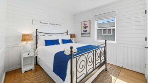 A bedroom with a bed, nightstand, and a window with a view. - Blue Bungalow | 625 ft from the beach | Hot Tub, Dog Friendly | Kitty Hawk (Kitty Hawk)