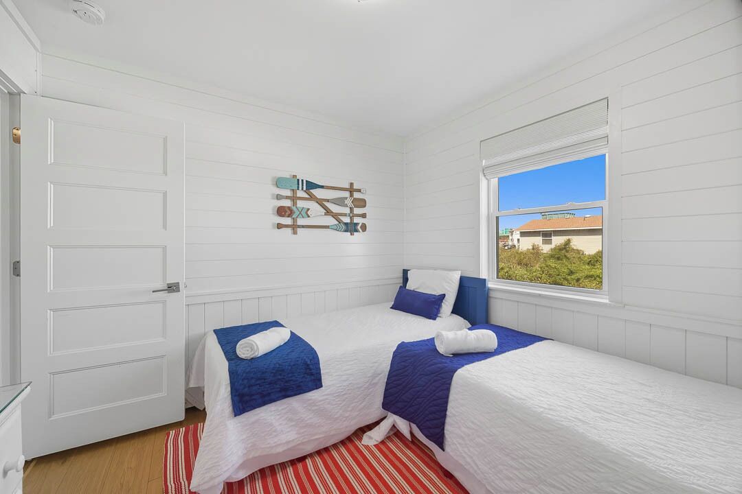 A room with two beds, a window with a view, a door, and a wall-mounted decoration.