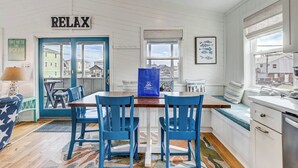 A cozy kitchen with a dining area, featuring a 'RELAX' sign, a view through the window, and a blue bag on the table. - Blue Bungalow | 625 ft from the beach | Hot Tub, Dog Friendly | Kitty Hawk (Kitty Hawk)