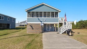 A two-story building with a blue exterior, a front entrance, and an American flag. - Blue Bungalow | 625 ft from the beach | Hot Tub, Dog Friendly | Kitty Hawk (Kitty Hawk)