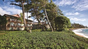 Um hotel à beira-mar com várias varandas, um jardim bem cuidado e vista para o oceano.